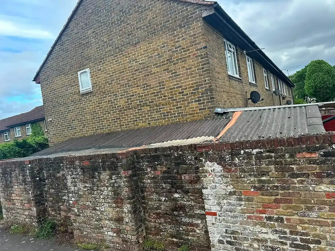 Brick house with several windows and satellite dishes behind an old brick wall and corrugated roof.
