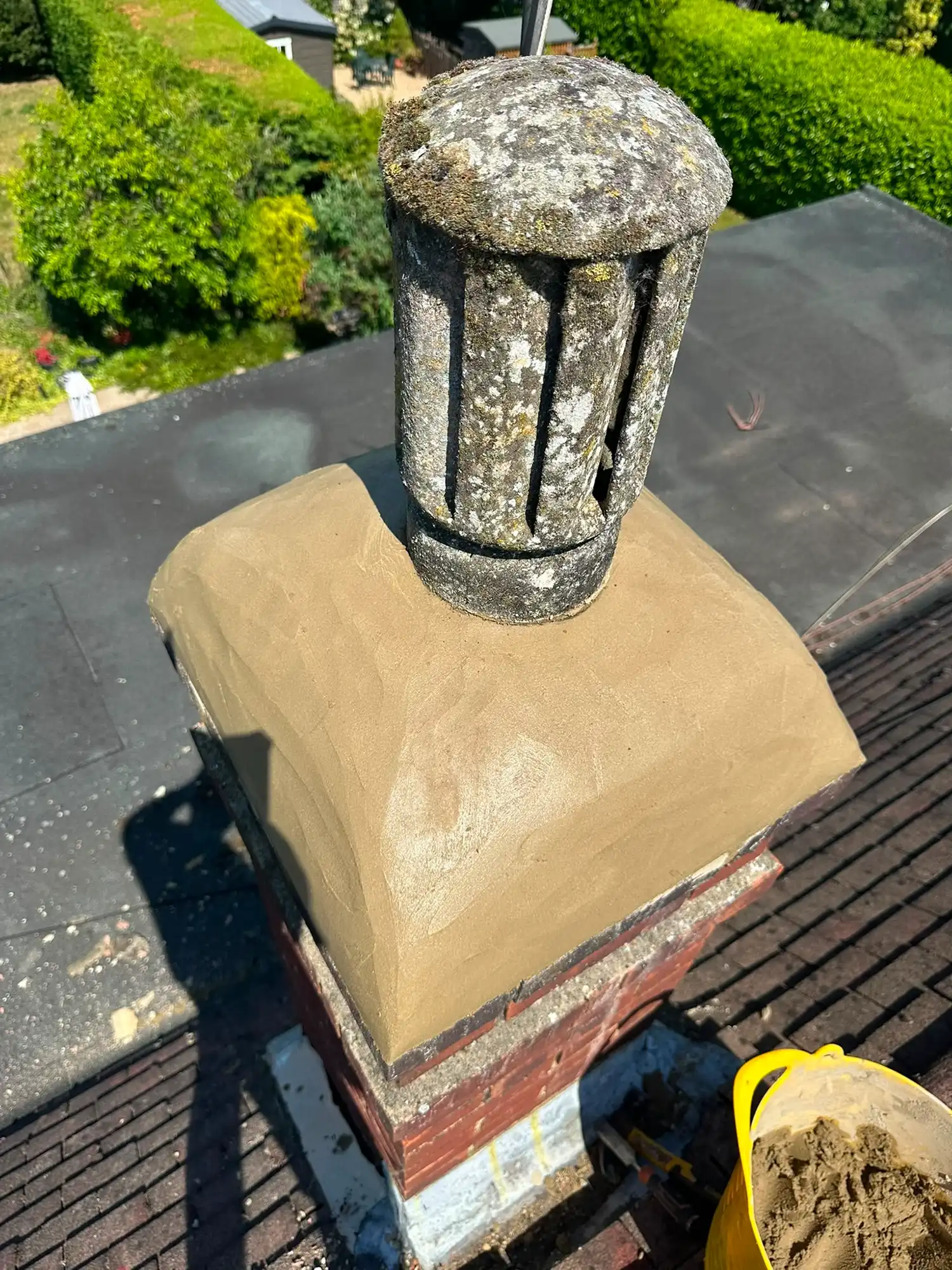 Freshly rendered chimney with a weathered cylindrical stone chimney pot on a rooftop.
