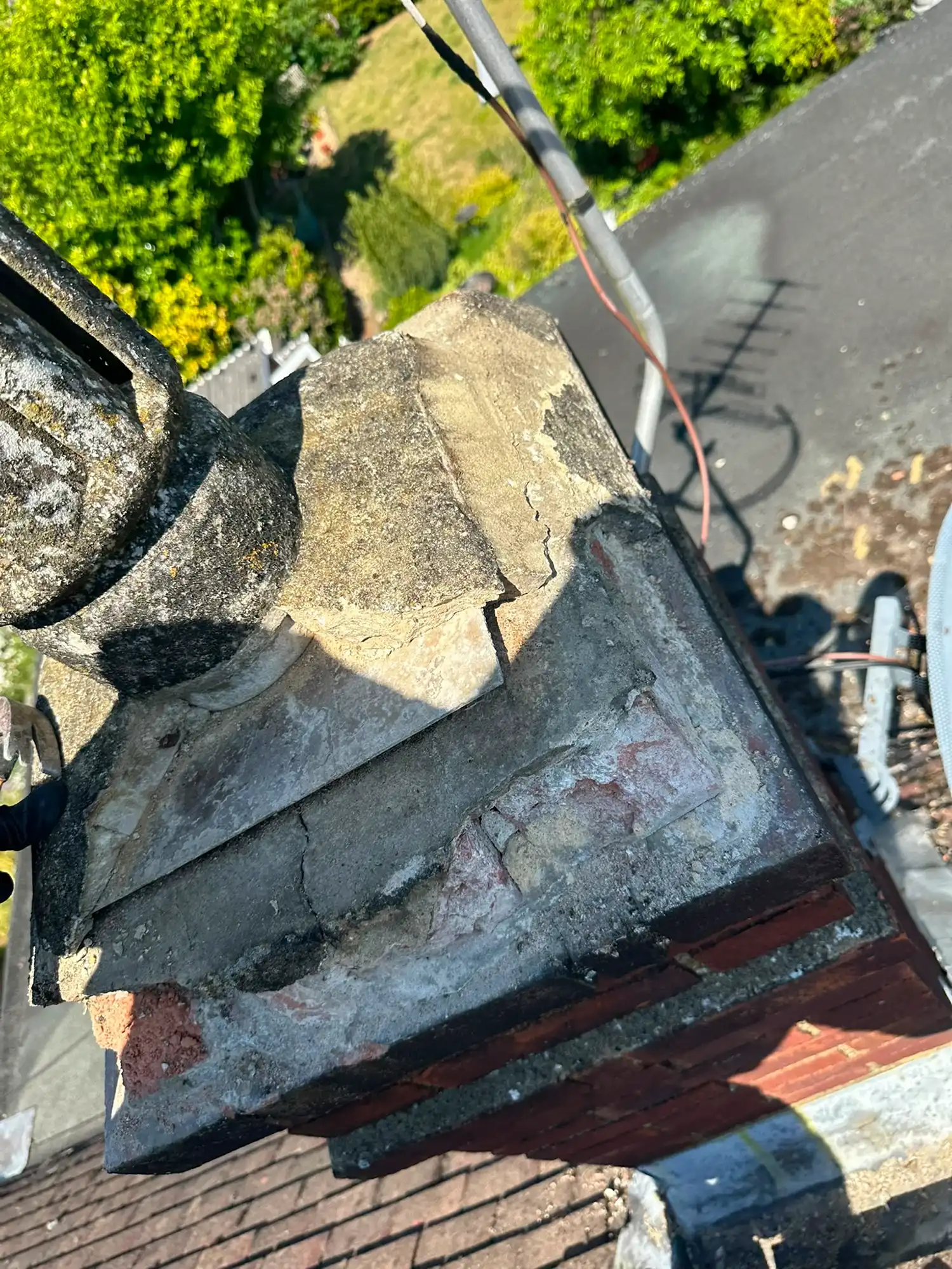 Close-up of a damaged rooftop chimney with cracked and crumbling concrete crown.