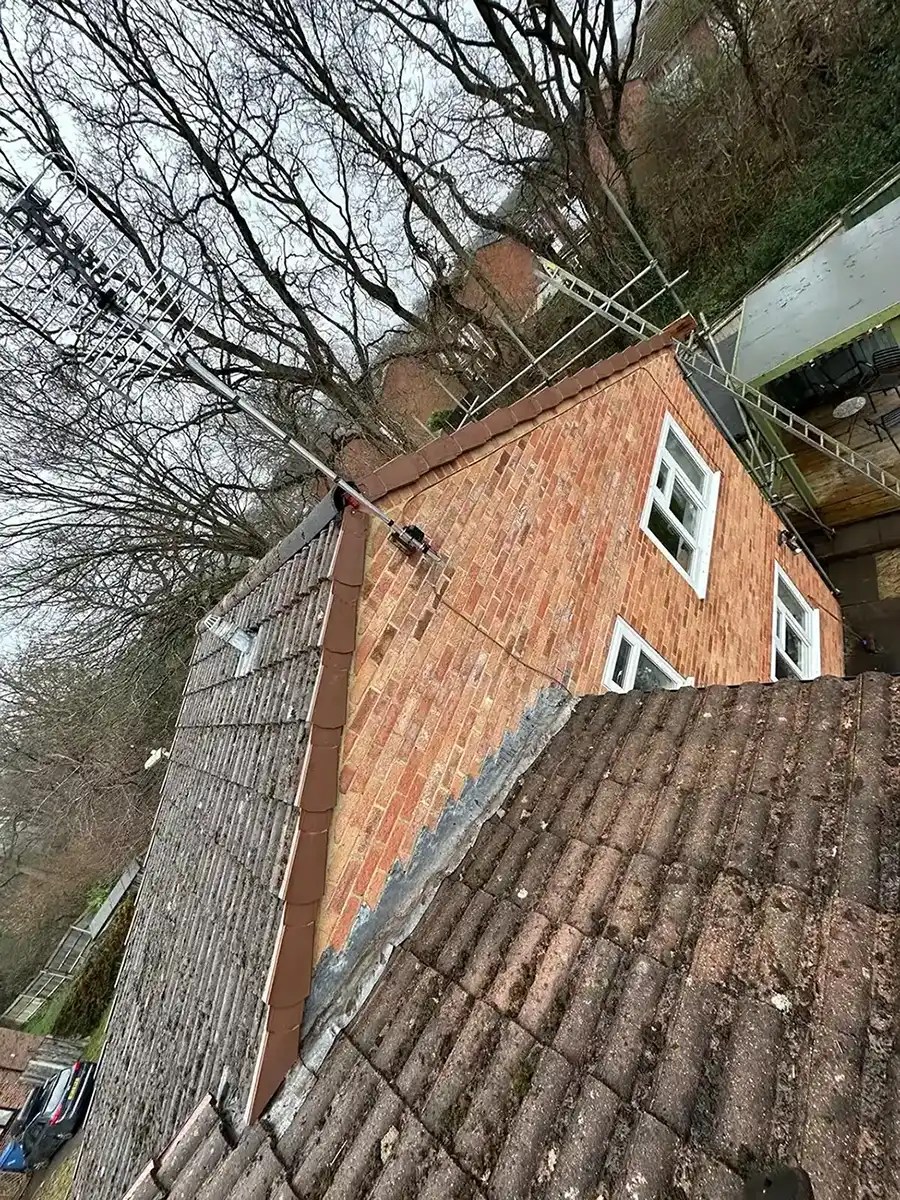 View of a brick house roof with a large TV antenna mounted and leafless trees in the background.