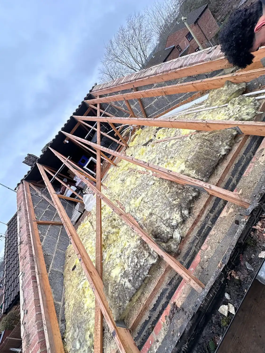 Partial roof frame with exposed wooden trusses and yellow insulation laid on the ceiling.