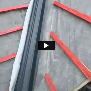 Close-up of roof under construction with red wooden battens and black ridge vent on gray shingles.