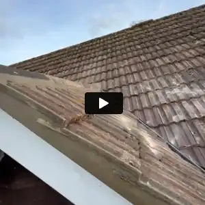 Close-up of a tiled roof section with a ridge and overlapping roof tiles under a blue sky.