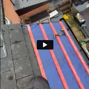 A rooftop under construction with blue and red waterproofing membrane and tools scattered on it.